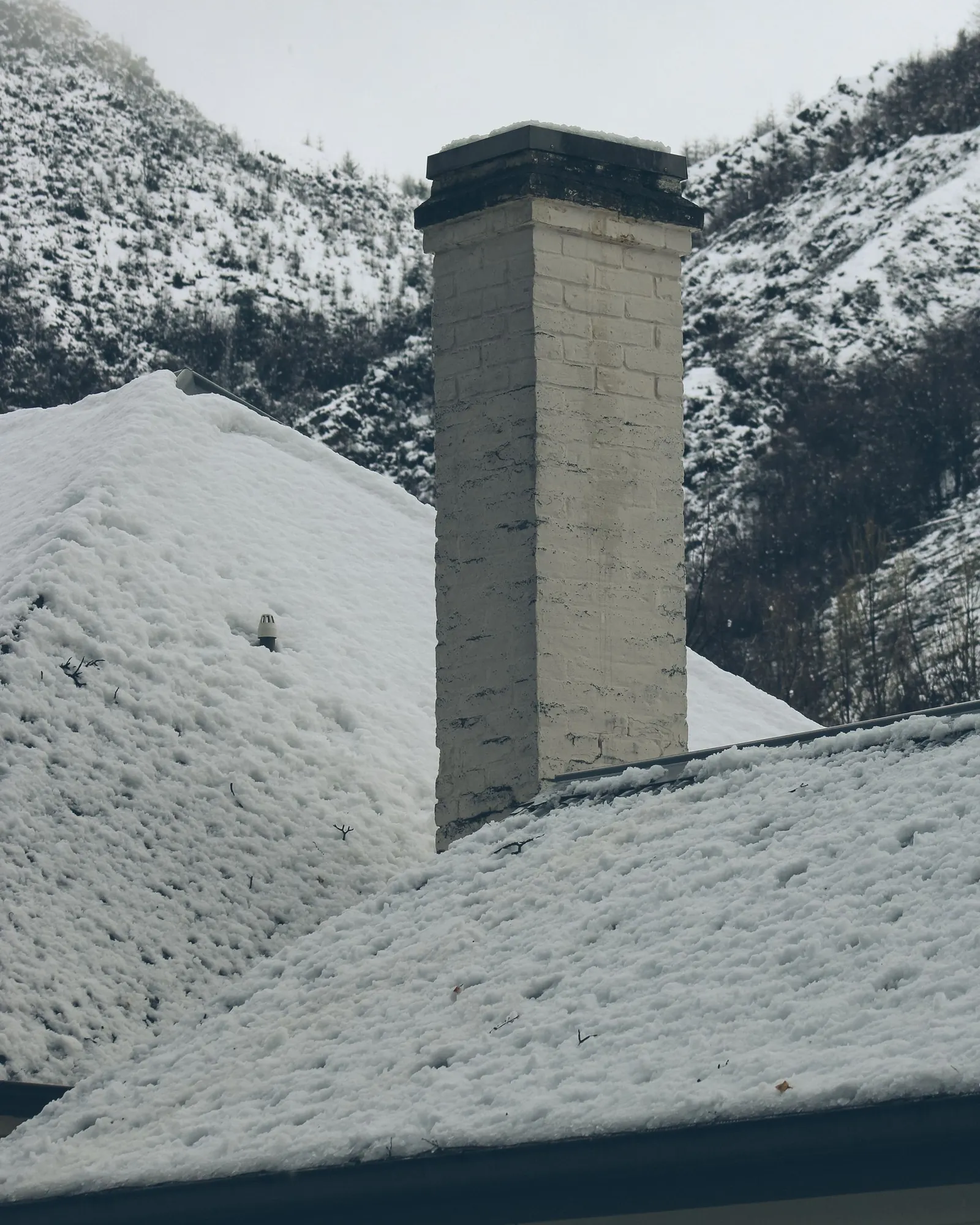 Tall chimney on a snow-covered roof with snowy mountain slopes behind
