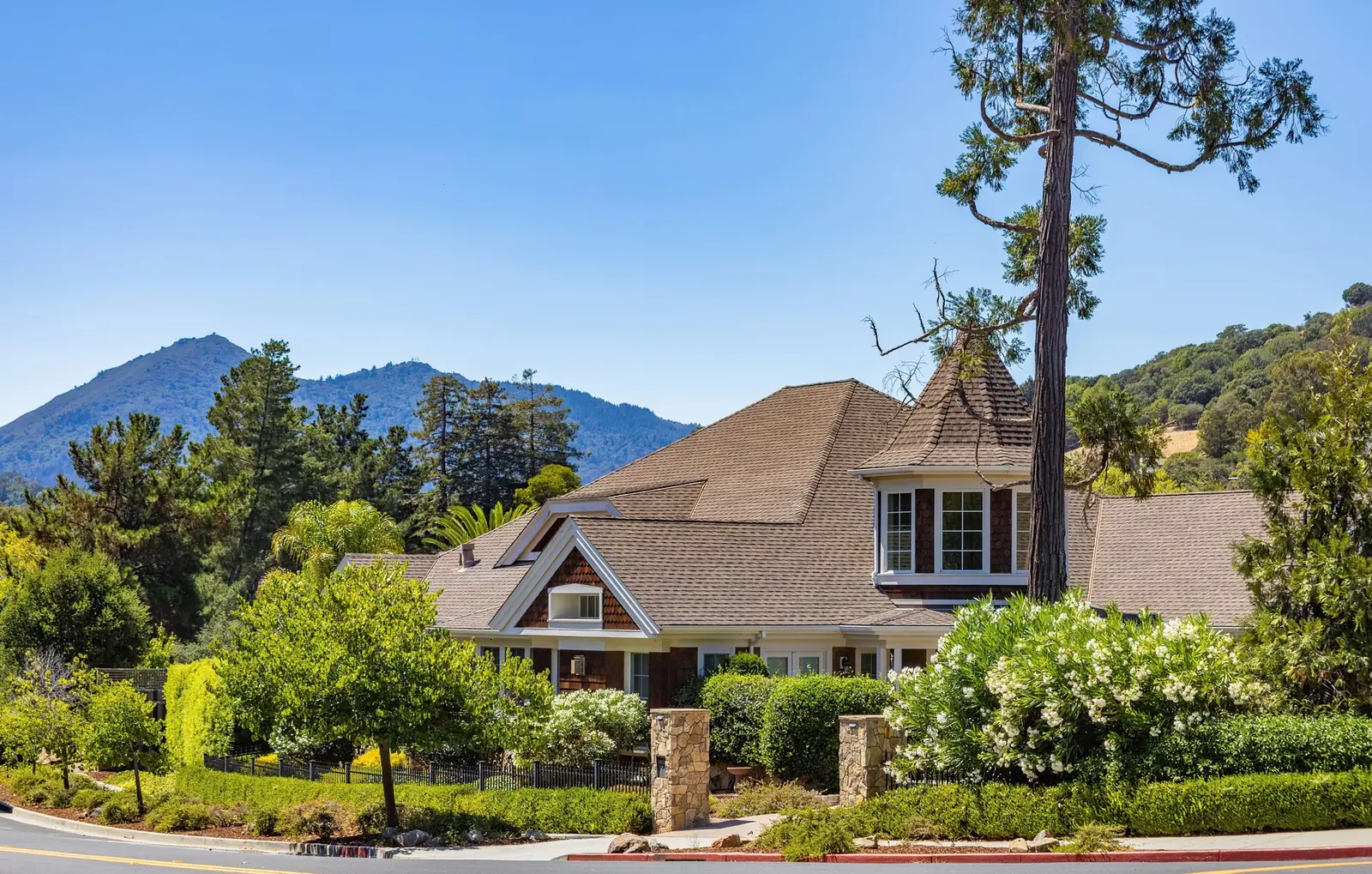 Large shingled home among gardens and pines with foothills behind it