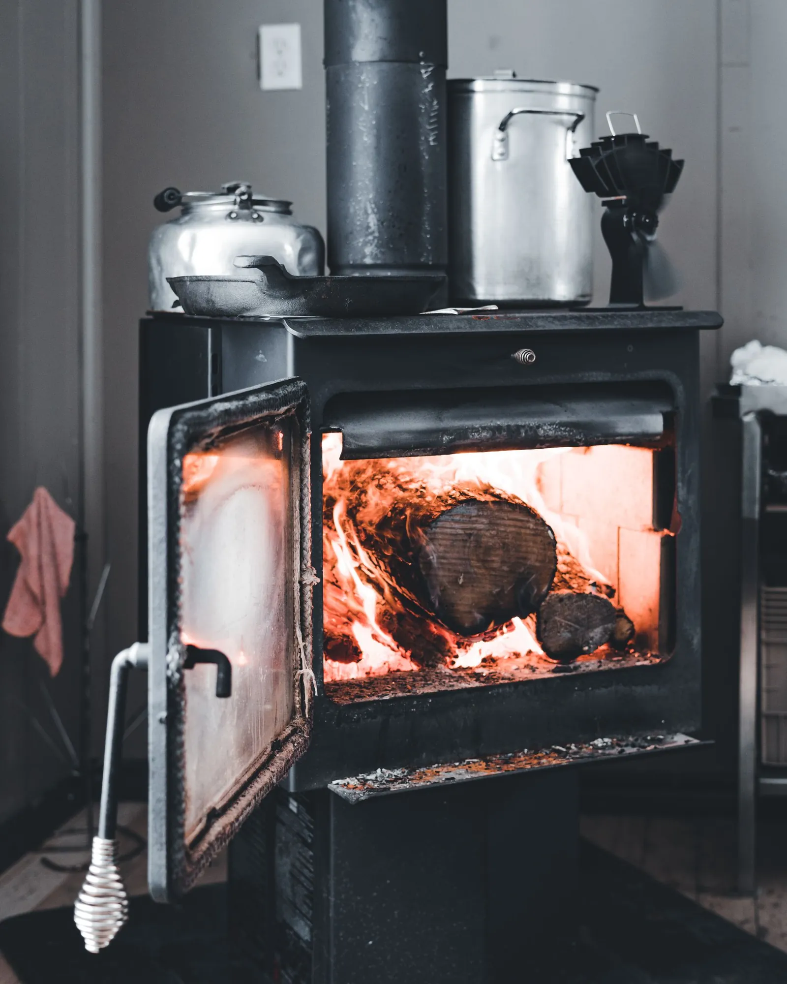 Black cast-iron wood stove with door open and a log burning inside